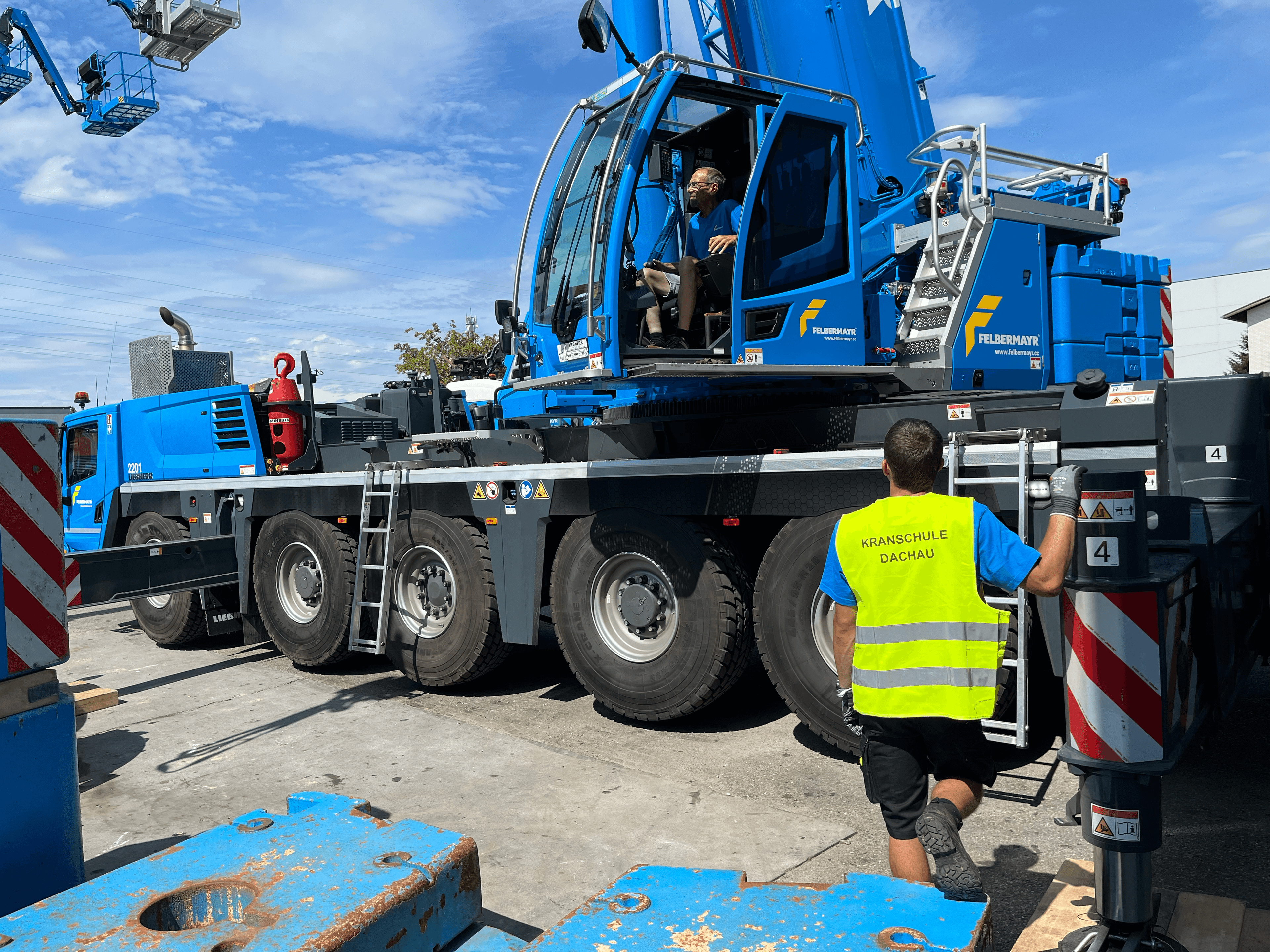 Ein Ausbilder der Kranschule Dachau gibt Anweisungen neben einem großen blauen Kran.