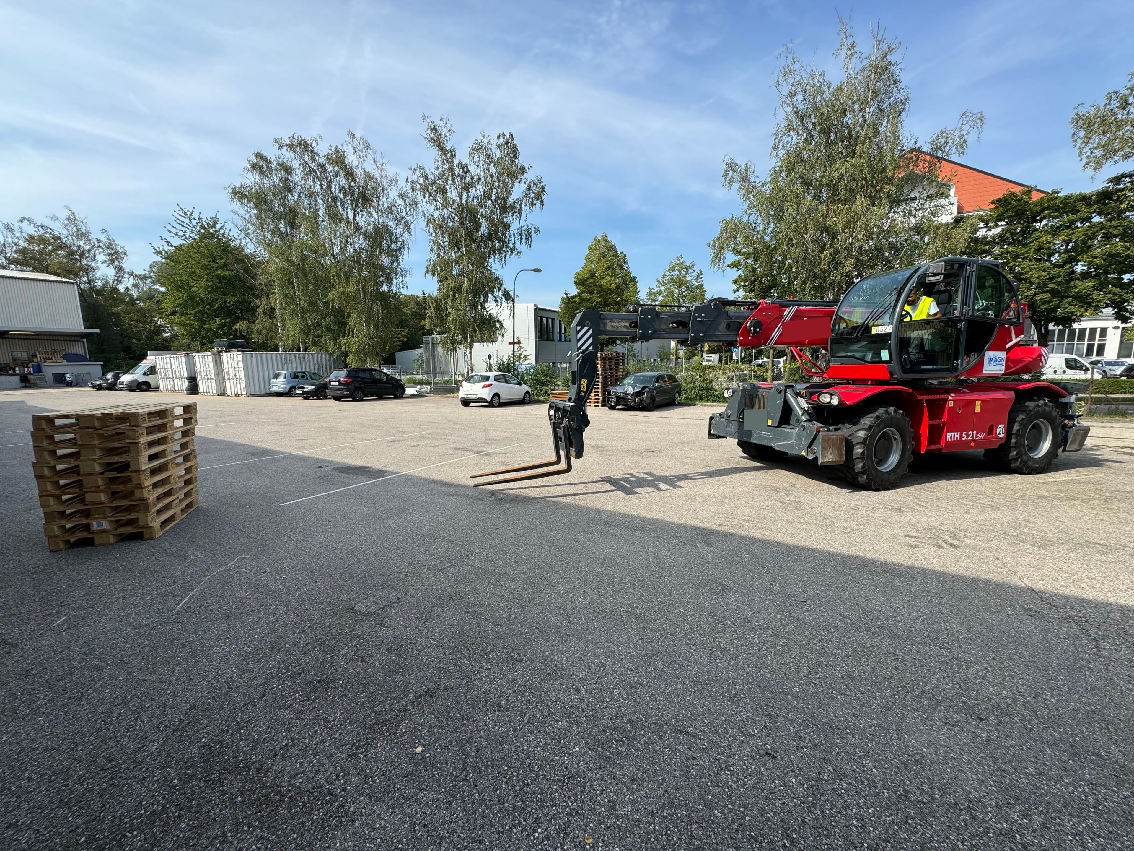 Roter Teleskopstapler teleskopiert die Gabeln zu einem Stoß Paletten im Freien