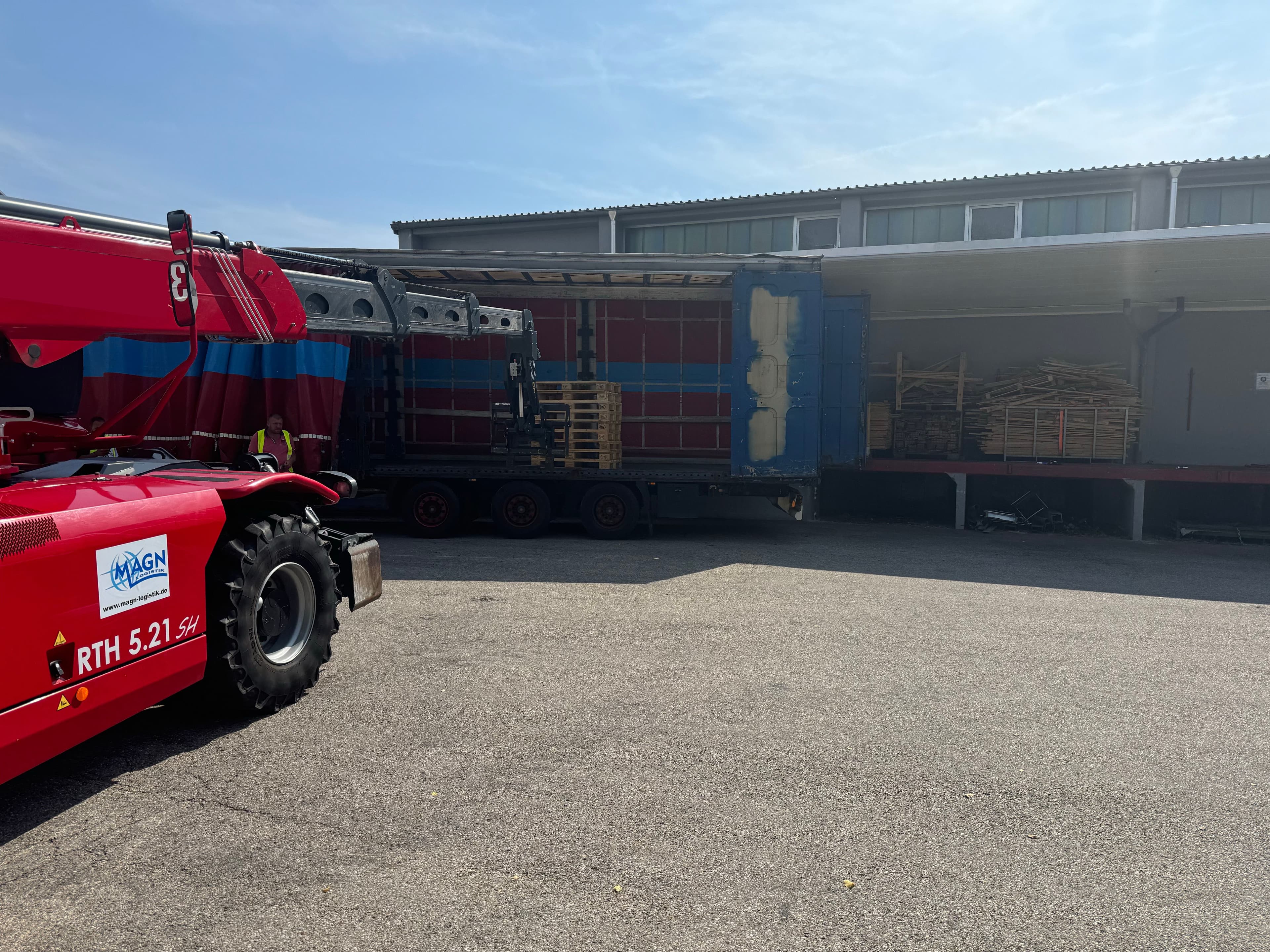 Roter Teleskopstapler teleskopiert Paletten in einen Auflieger.