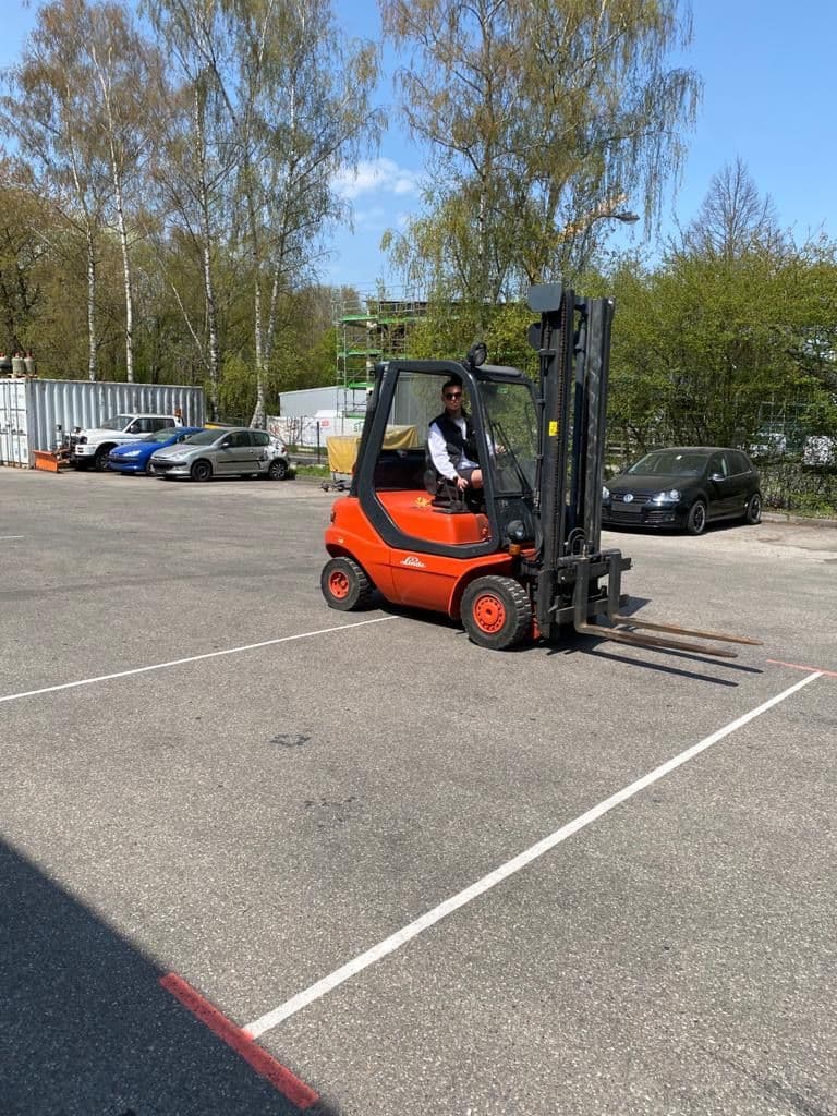 Arbeiter in orangener Sicherheitskleidung fährt einen Gabelstapler und transportiert Abfallmaterialien auf einer Baustelle.