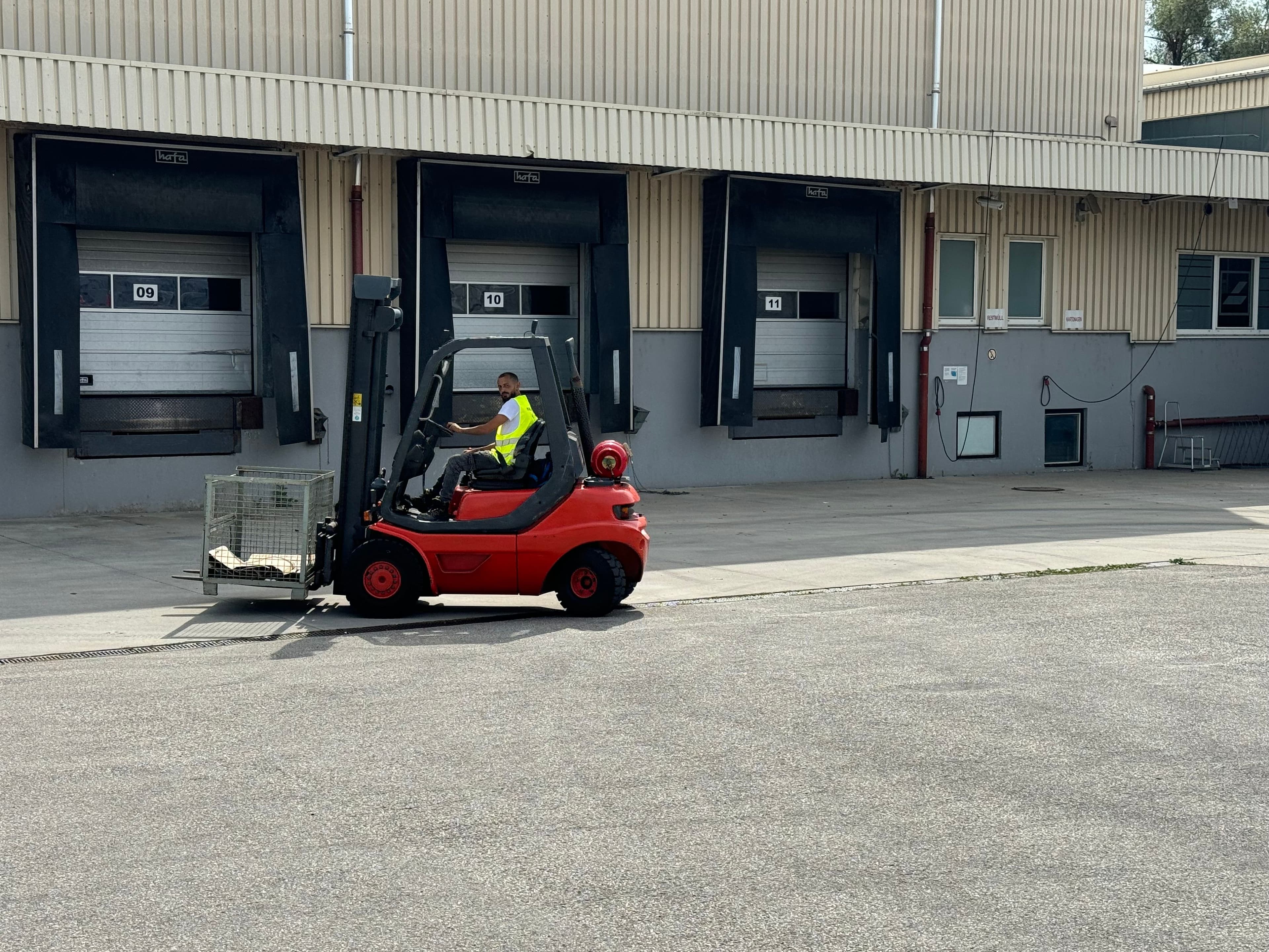 Roter Gabelstapler transportiert eine Gitterbox mit einem Fahrschüler