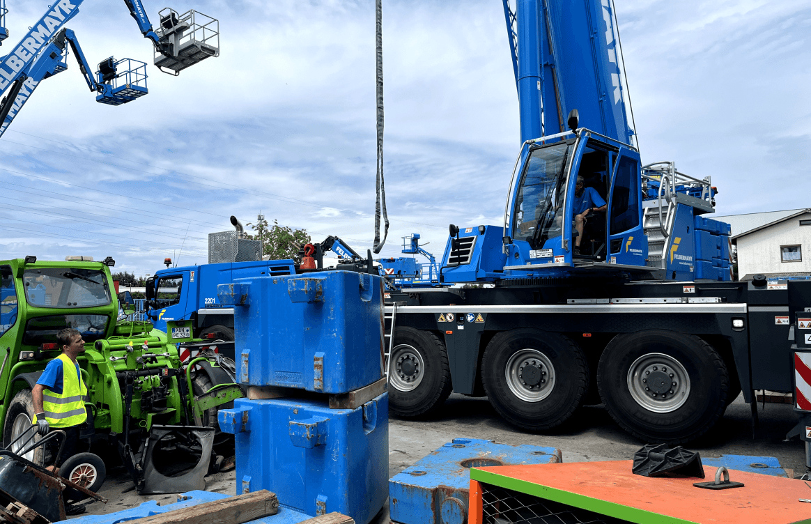 Großer blauer Kran im Einsatz auf einer Baustelle, Arbeiter in der Nähe eines grünen Fahrzeugs