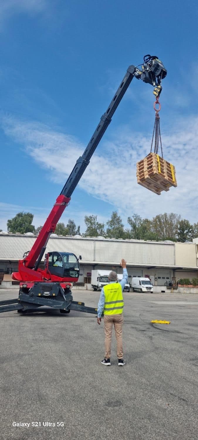 Teleskopstapler schwenkt Paletten unter Aufsicht eines Anschlägers