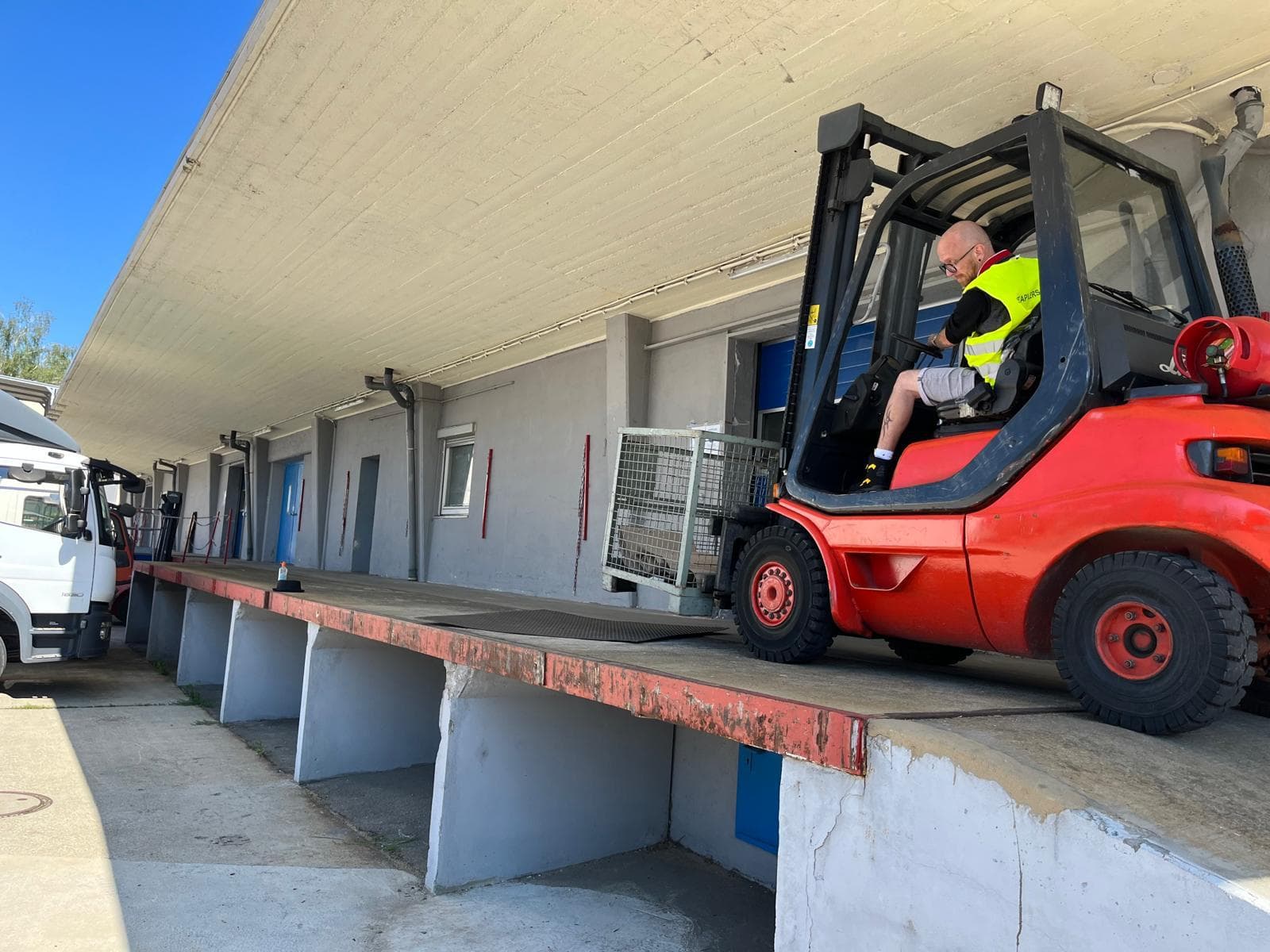 Gabelstaplerfahrer lädt einen Metallkorb auf eine Laderampe, umgeben von Lkws.